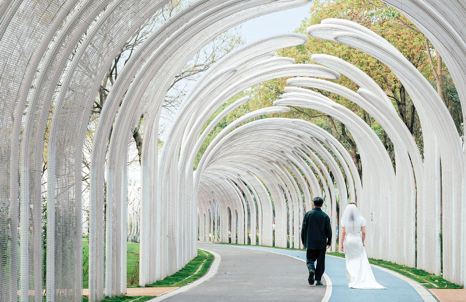 A bride and groom walking through a tunnel of white arches