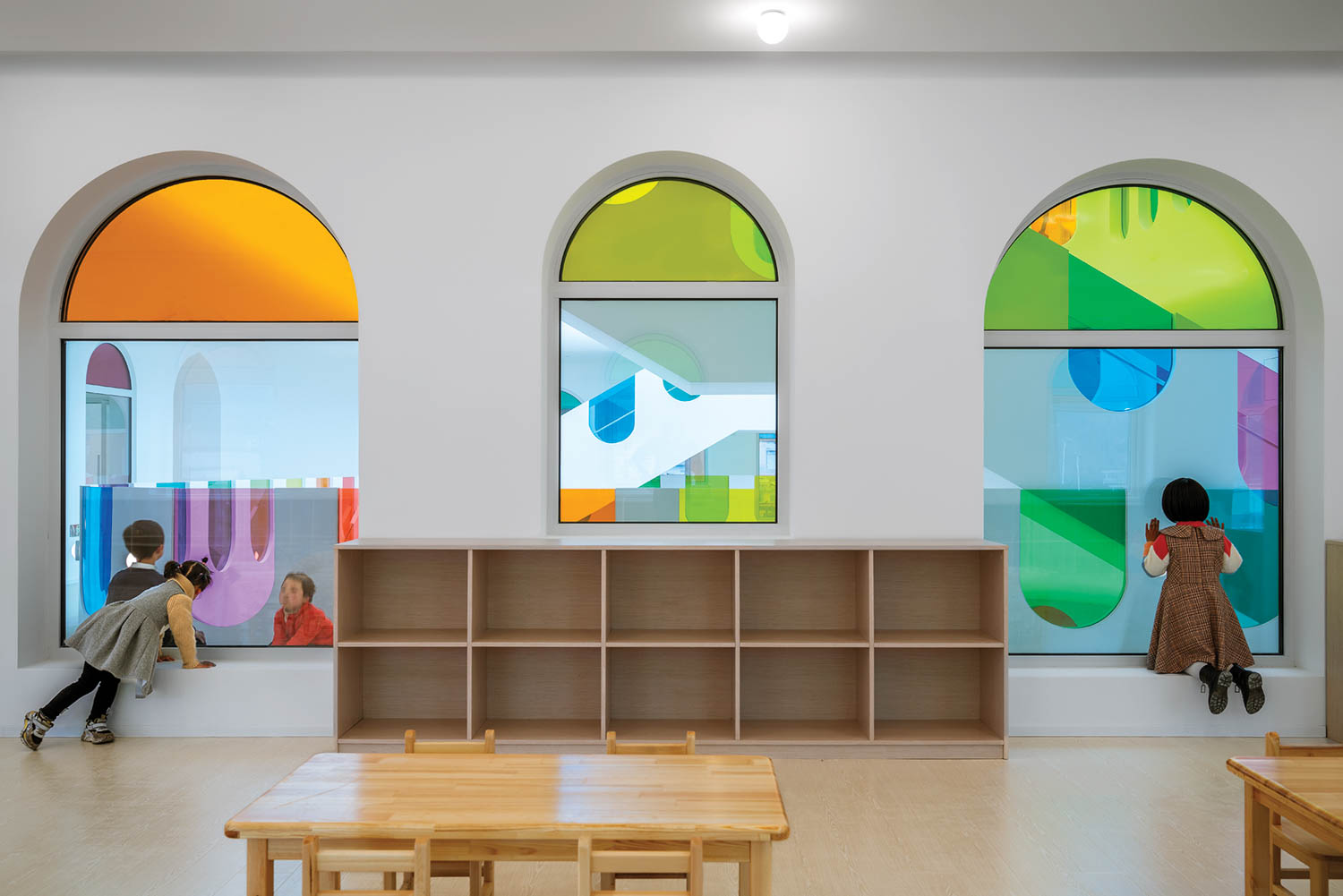 children play in cubbies framed by rainbow hued windows