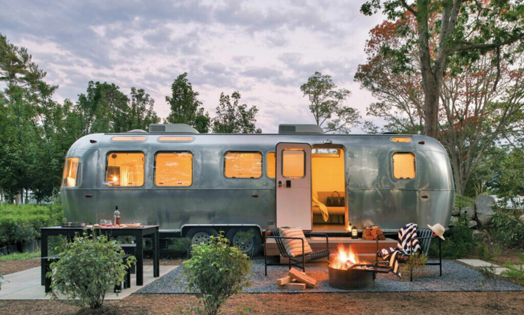 an airstream in the woods with firepit