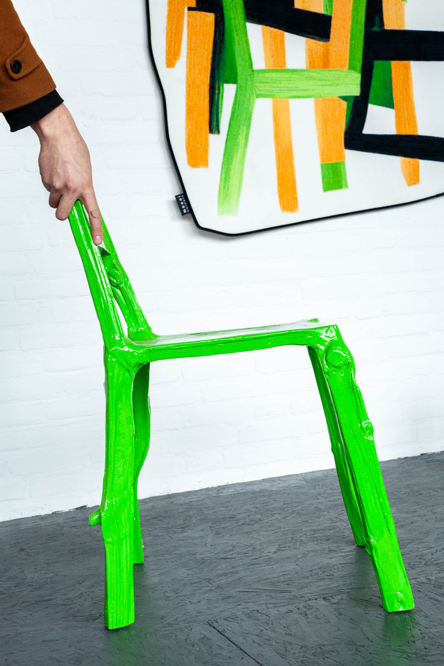 bright neon green chair underneath an abstract painting made of orange and black paint