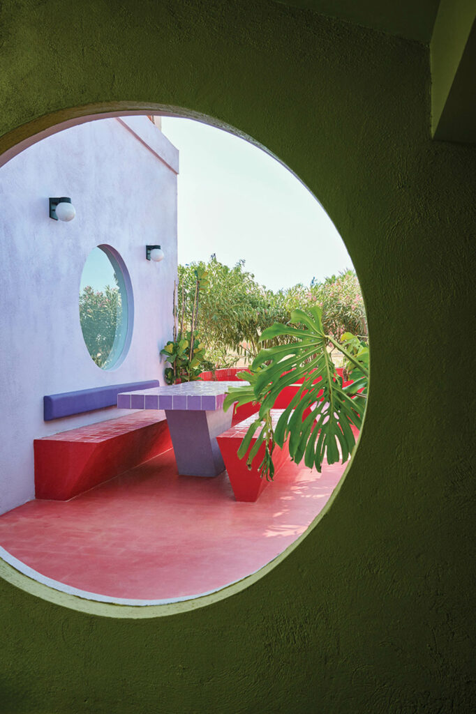 view through circular window with outdoor benches and red tables