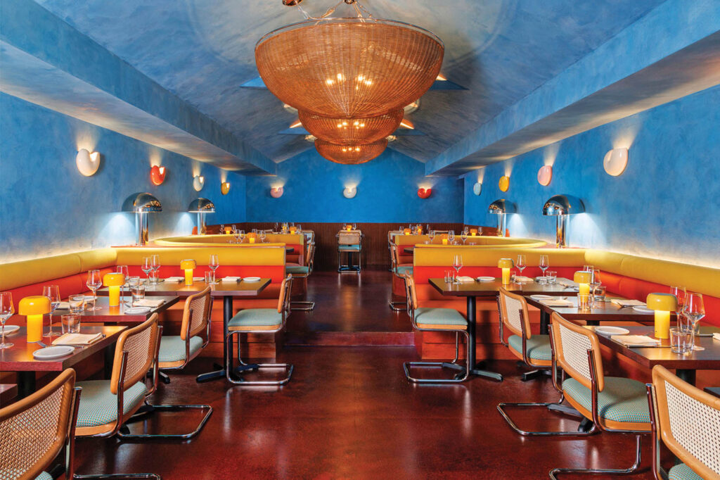 dining room with blue limewash walls, basketlike chandeliers and colorful sconces and chairs