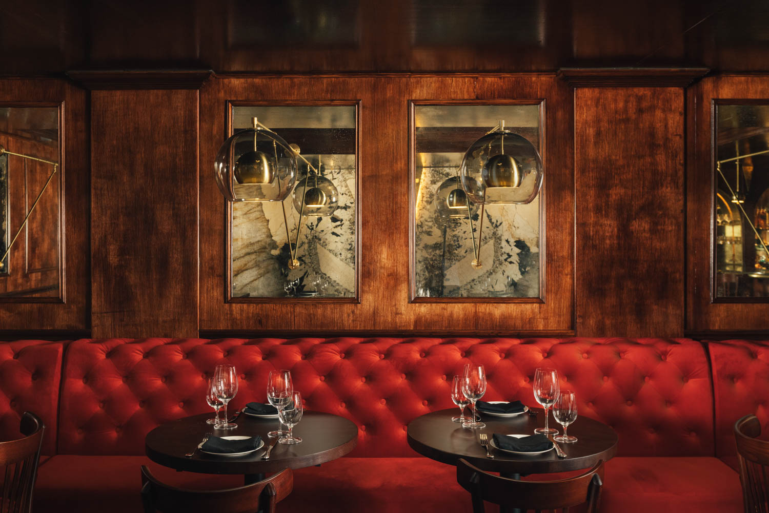 the antique mirrors on the wooden paneled walls hanging above the red banquette