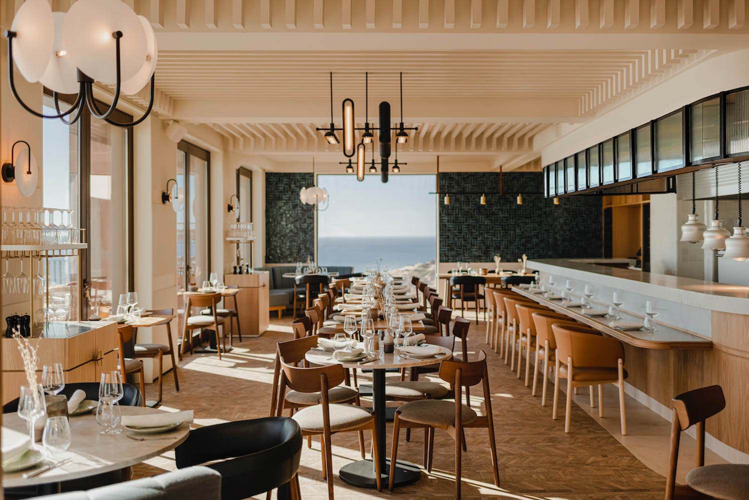 Onda restaurant with lots of wooden chairs, chandelier, black tile walls and ocean views