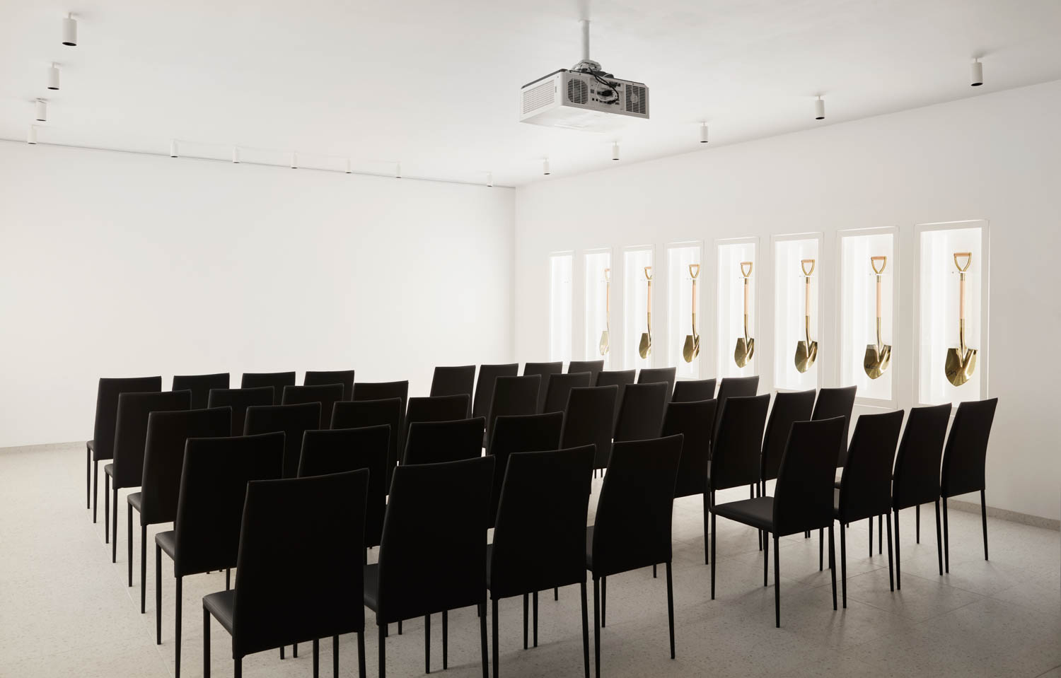 room with multiple black chairs in a row and golden shovels hanging on display