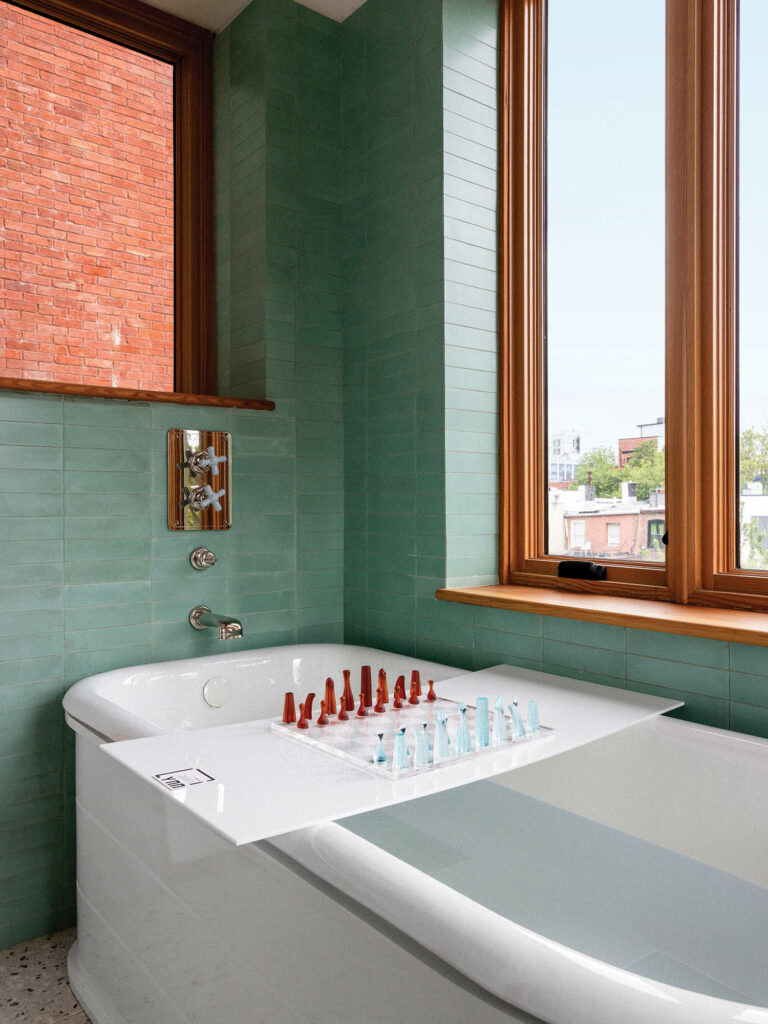 bathroom with sage green tiles, white porcelain tub and a chess set lying across