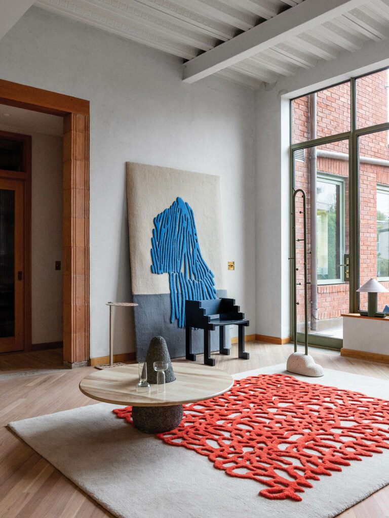 living room with red lattice artwork on top of white rug, brown circular table and artwork with blue lattice pattern