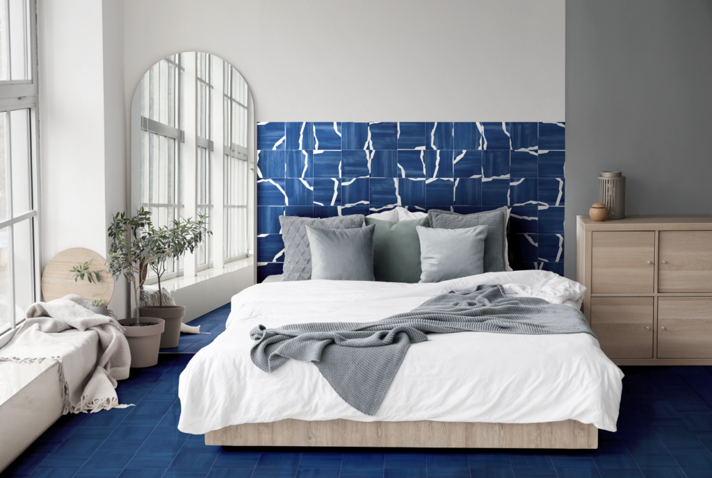 bedroom with dark blue tile backdrop and matching rug and white bed with silver pillows